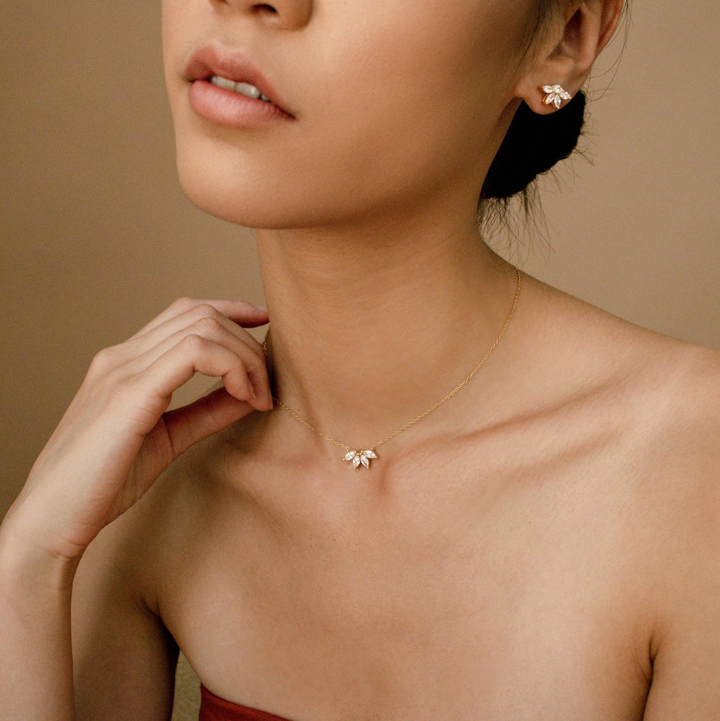 Marquise diamond stud earrings in 18K gold worn with matching delicate marquise diamond pendant necklace on a model against.