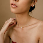 Marquise diamond stud earrings in 18K gold worn with matching delicate marquise diamond pendant necklace on a model against.