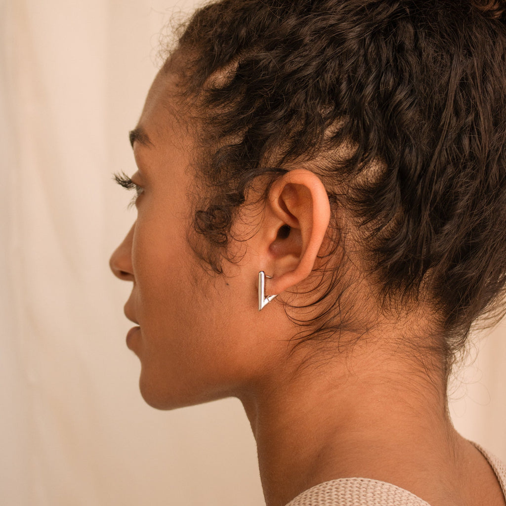 A woman with curly hair wears Triangle Huggies in her left ear, adding a chic touch to her summer style.