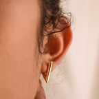 Close-up of a person's ear wearing sleek gold Triangle Huggies; curly hair partly visible—these geometric earrings are perfect for bold summer style.