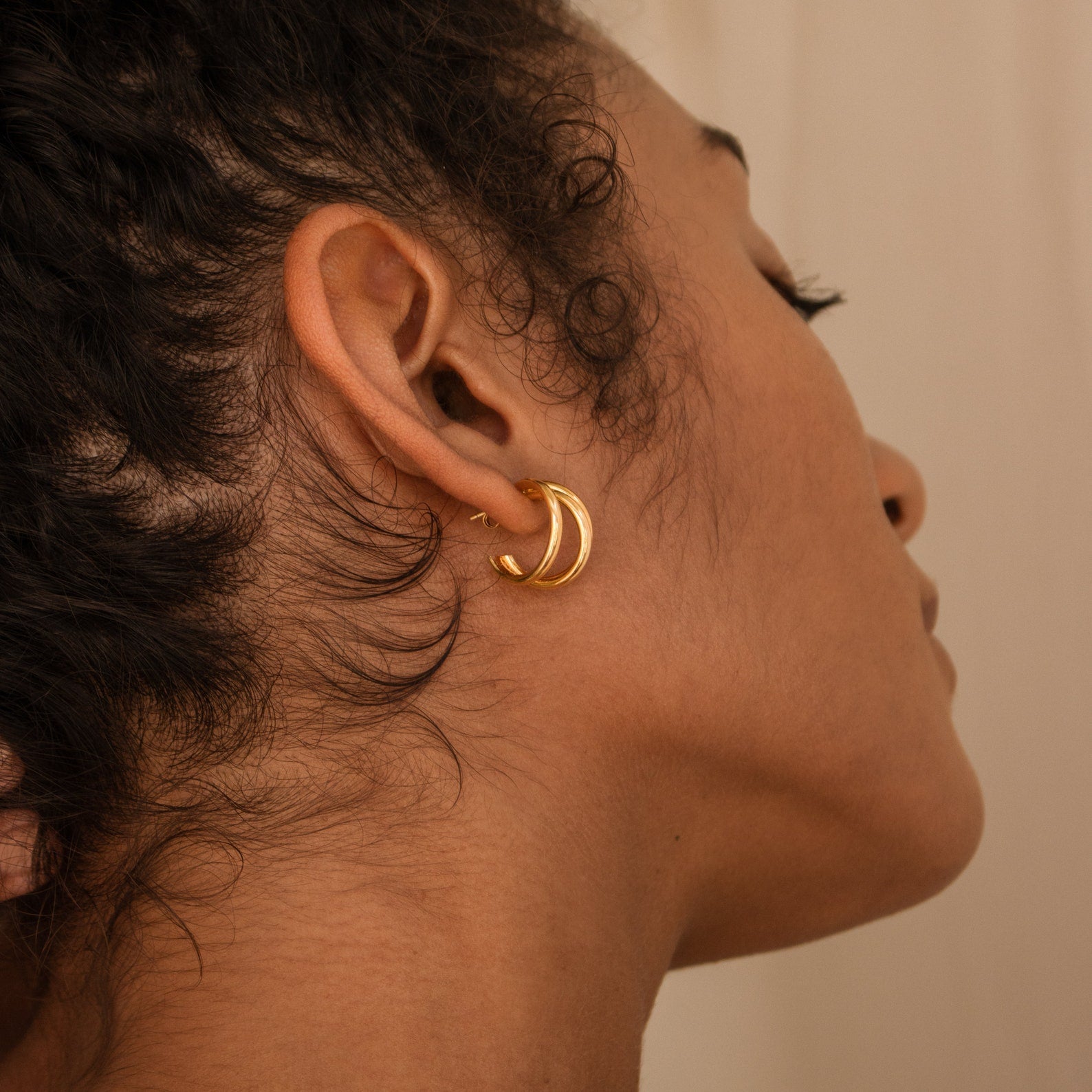 Close-up of a woman's ear wearing Jenna Triple Hoops, thick gold earrings with curls framing her minimalist style.