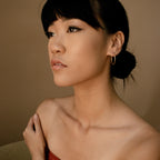 A woman with dark hair in a low bun, wearing Medium Thin Hoops, gazes thoughtfully to the side.