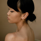 A woman with dark hair in a low bun wears Endless Thin Hoops, posing against a tan background—highlighting these timeless hoops as the ideal everyday accessory.