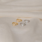 Four heart-shaped rings, two gold and two silver, rest on soft cream fabric, echoing the timeless charm of Scarlett Pearl Huggies and capturing the elegance found in classic mother of pearl heart jewelry.
