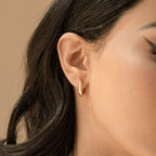 Close-up of a woman's ear adorned with Madison Hoops, featuring minimalist gold design, visible dark hair, and winged eyeliner.