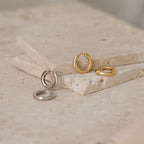 Two pairs of Madison Hoops, one gold and one silver, displayed on stacked stone slabs for a minimalist touch.