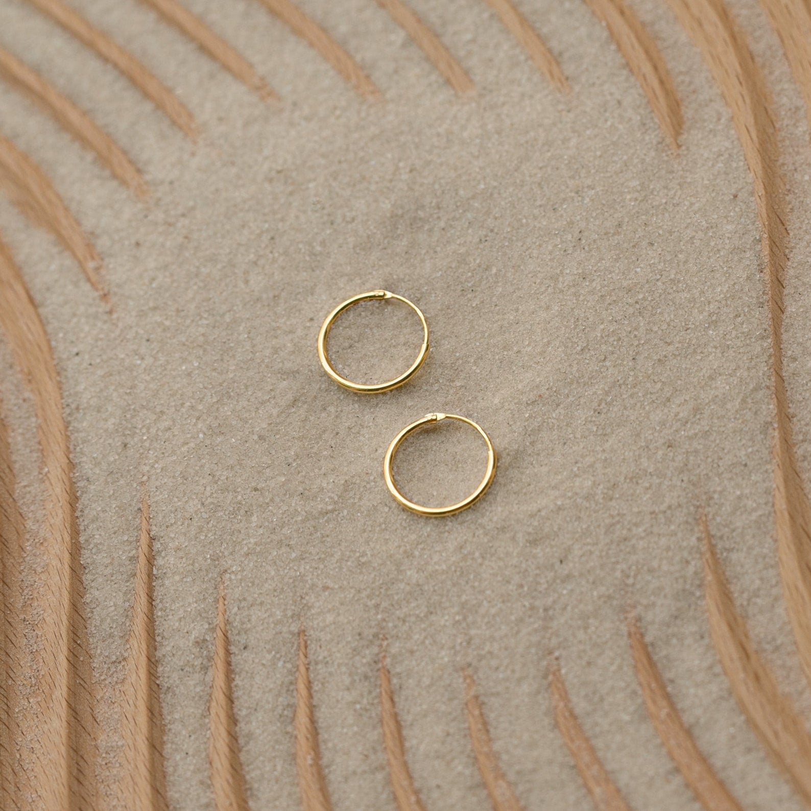 Small Thin Hoops set on textured sand with wavy wood patterns make the perfect simple addition to your everyday jewelry collection.