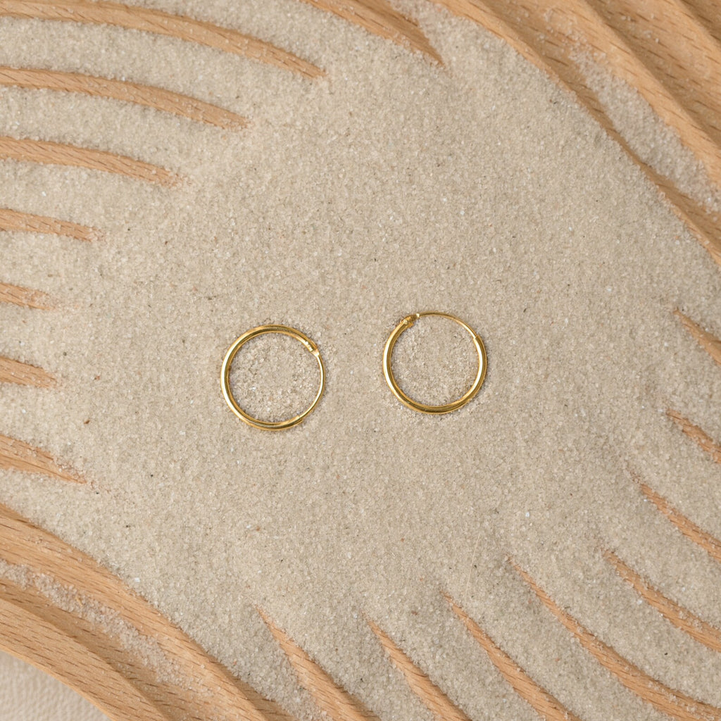 Endless Thin Hoops rest on sand with wooden patterns, offering a timeless earring style that’s perfect for everyday wear.