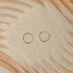 Endless Thin Hoops rest on sand with wooden patterns, offering a timeless earring style that’s perfect for everyday wear.