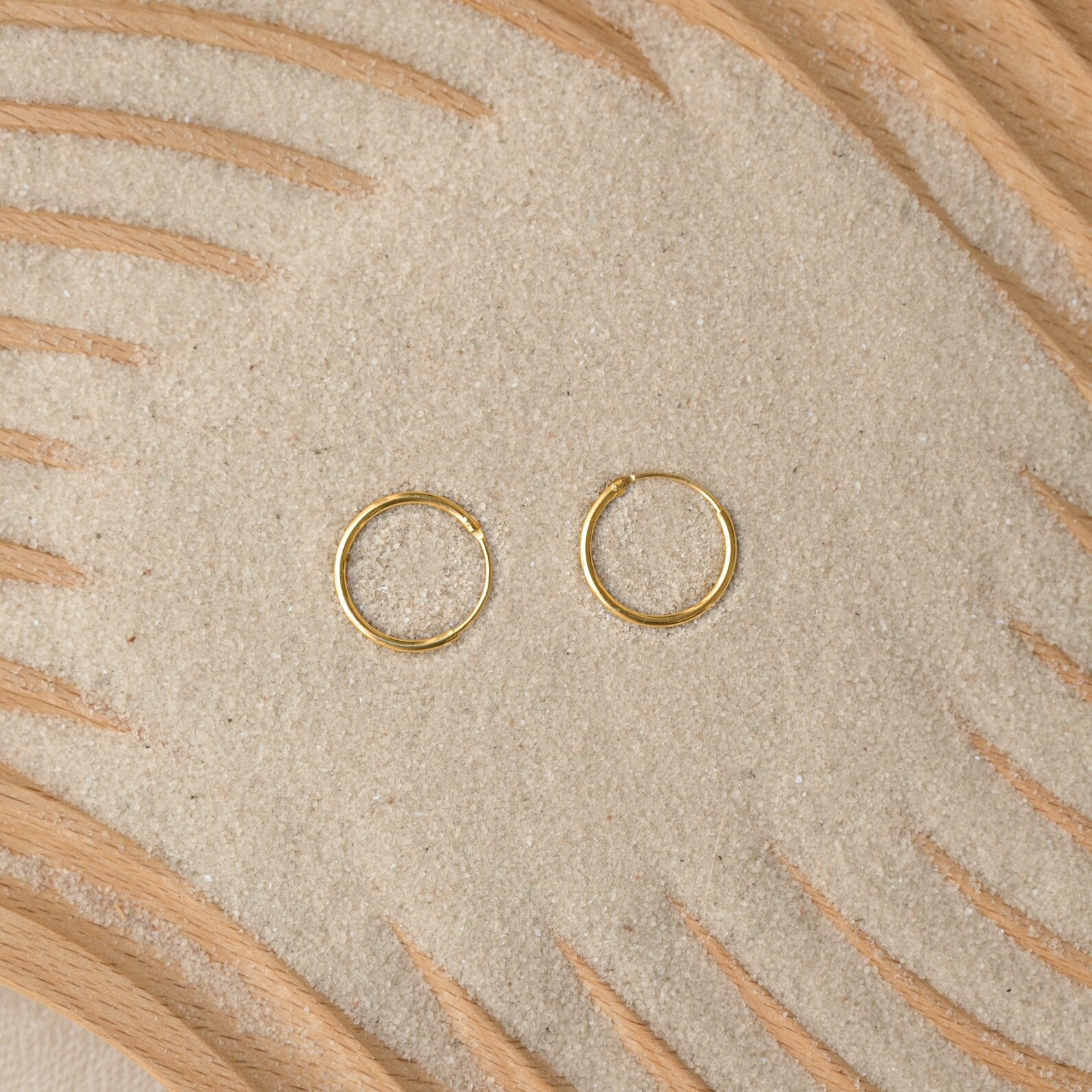 Endless Thin Hoops rest on sand with wooden patterns, offering a timeless earring style that’s perfect for everyday wear.