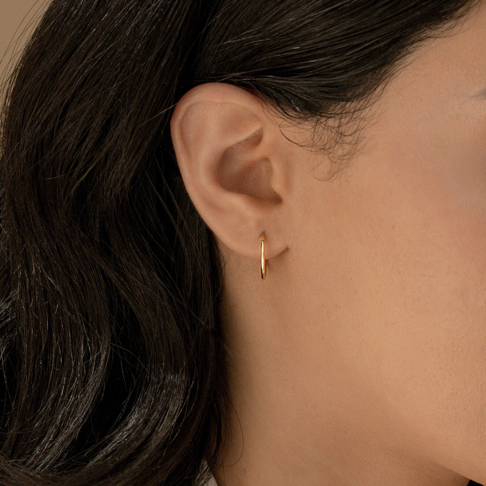 Close-up of a woman's ear with Small Thin Hoops, her dark hair tucked behind her ear—a subtle and elegant addition to everyday style.