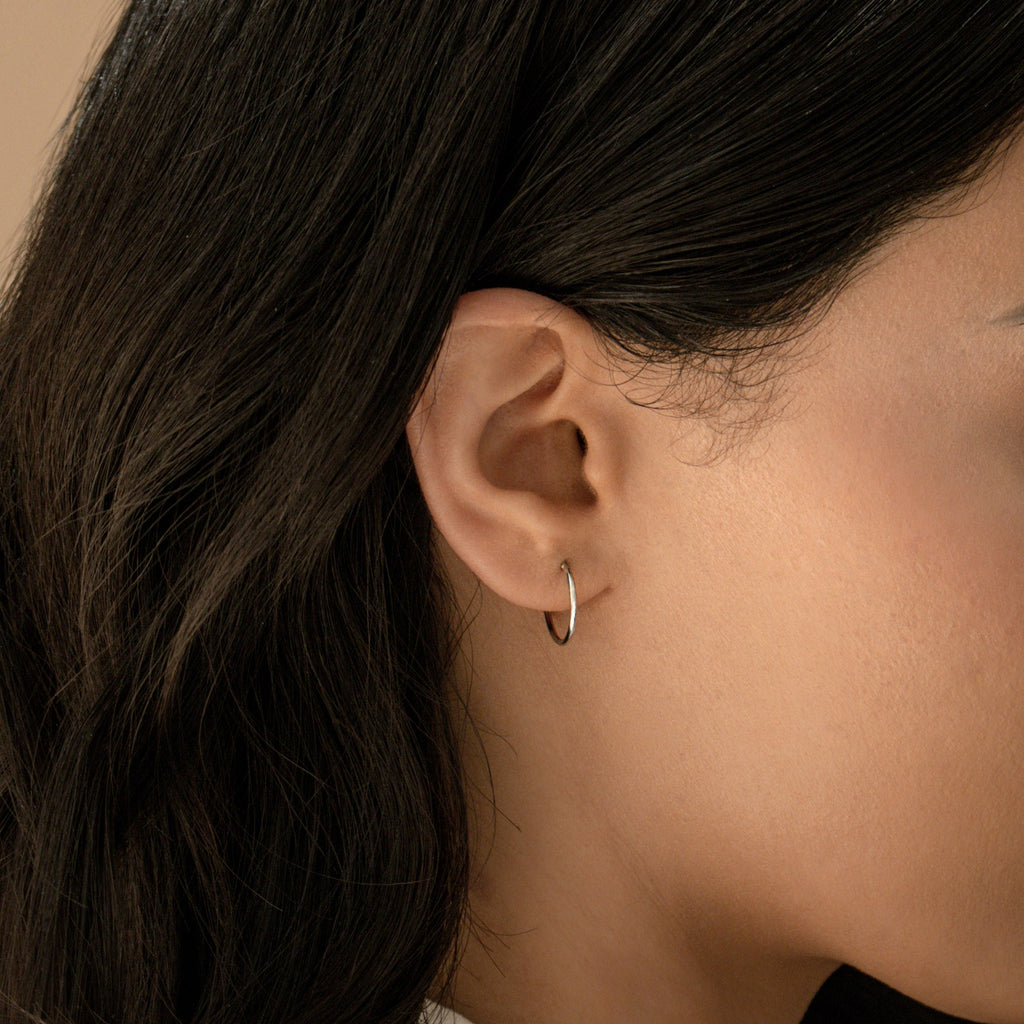 Close-up of a woman’s ear wearing Small Thin Hoops—simple earrings ideal for everyday wear—with dark hair draped behind her ear.