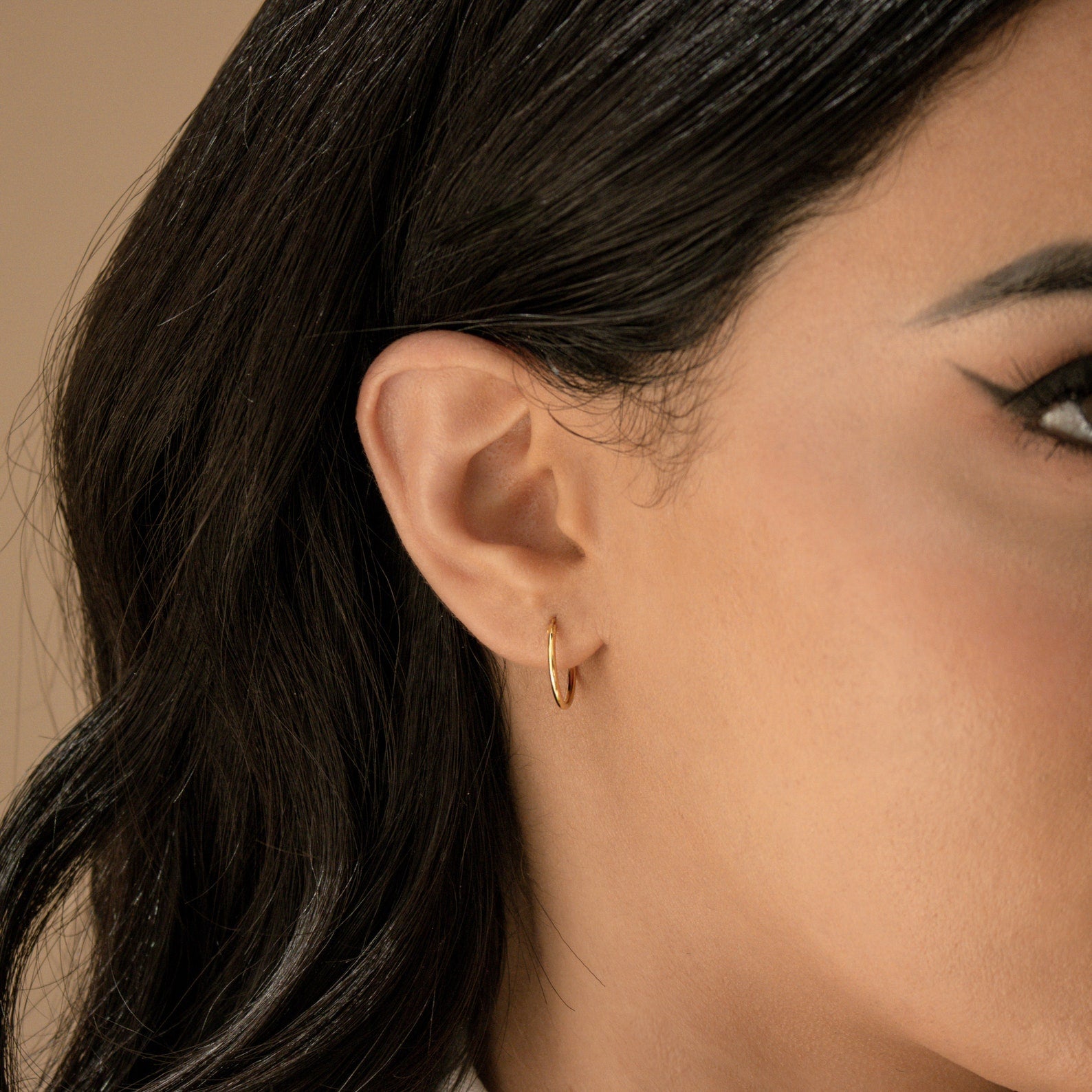 Close-up of a woman's ear with straight dark hair, wearing Small Thin Hoops—an elegant accessory for everyday style.