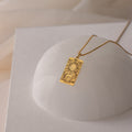 The Tarot Necklace in Box Chain features a gold rectangular pendant with a sun and celestial design inspired by the Major Arcana, shown on a white dome.
