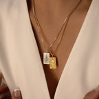 Close-up of a person wearing two Tarot Necklace in Box Chain pendants, one silver and one gold, over a white top—capturing the mystique of tarot cards and a touch of enigmatic charm.