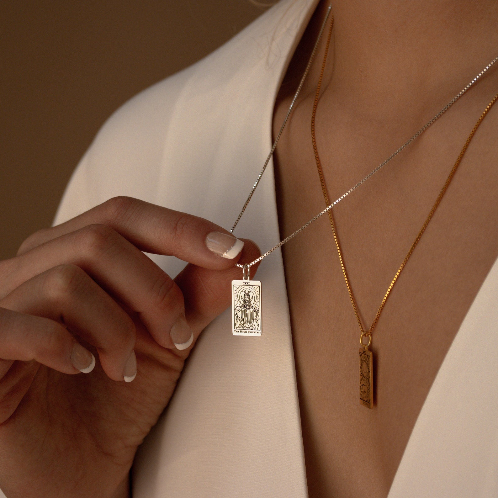 A woman in a white blouse holds the Tarot Necklace in Box Chain—its silver pendant layered above a gold chain, her style suggesting secrets inspired by the Major Arcana.