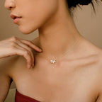 A close-up of a woman wearing a gold chain necklace with a central pendant featuring three marquise-cut diamonds arranged like a small floral cluster. She is posed gracefully with her hand near her collarbone, and her bare shoulders are framed against a neutral background.