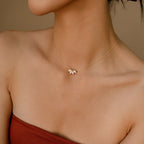 A minimalist shot of a woman’s neckline highlighting a delicate gold necklace with a trio of marquise diamonds in a symmetrical cluster design. The background is softly lit, and the model wears a strapless red top that complements the warm tones of the jewelry.