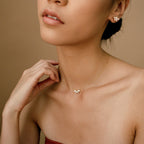 A stylish close-up of a woman wearing a matching jewelry set: a dainty gold necklace and stud earrings, both adorned with marquise-cut diamond clusters. Her hand gently touches her neck, emphasizing the elegant and feminine look of the coordinated set.