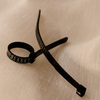 The Ring Sizer, a black cable tie with numbered markings for precise sizing, is placed on a textured beige fabric surface.