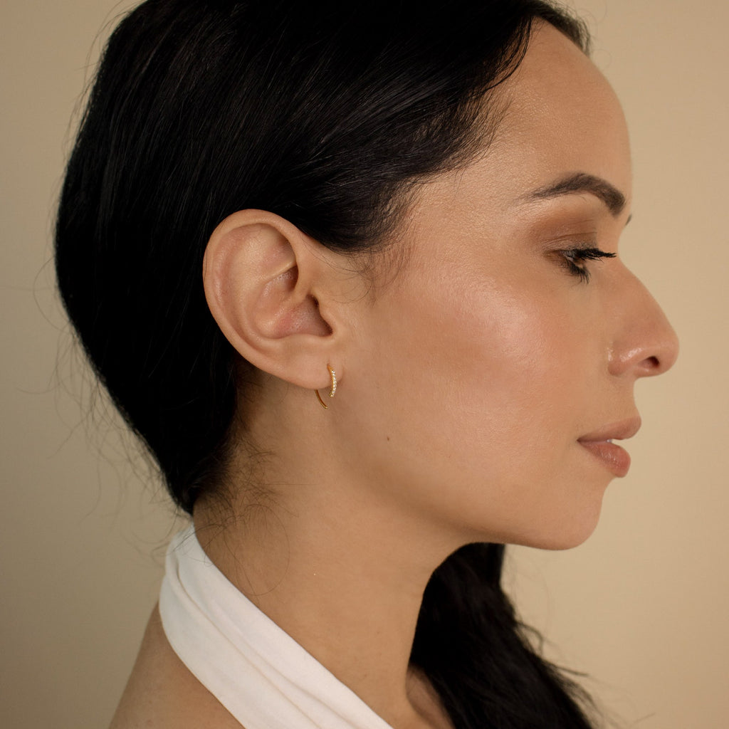 A woman with a white scarf around her neck wears Pave Wire Diamond Hoops, adding a touch of elegance to her look.