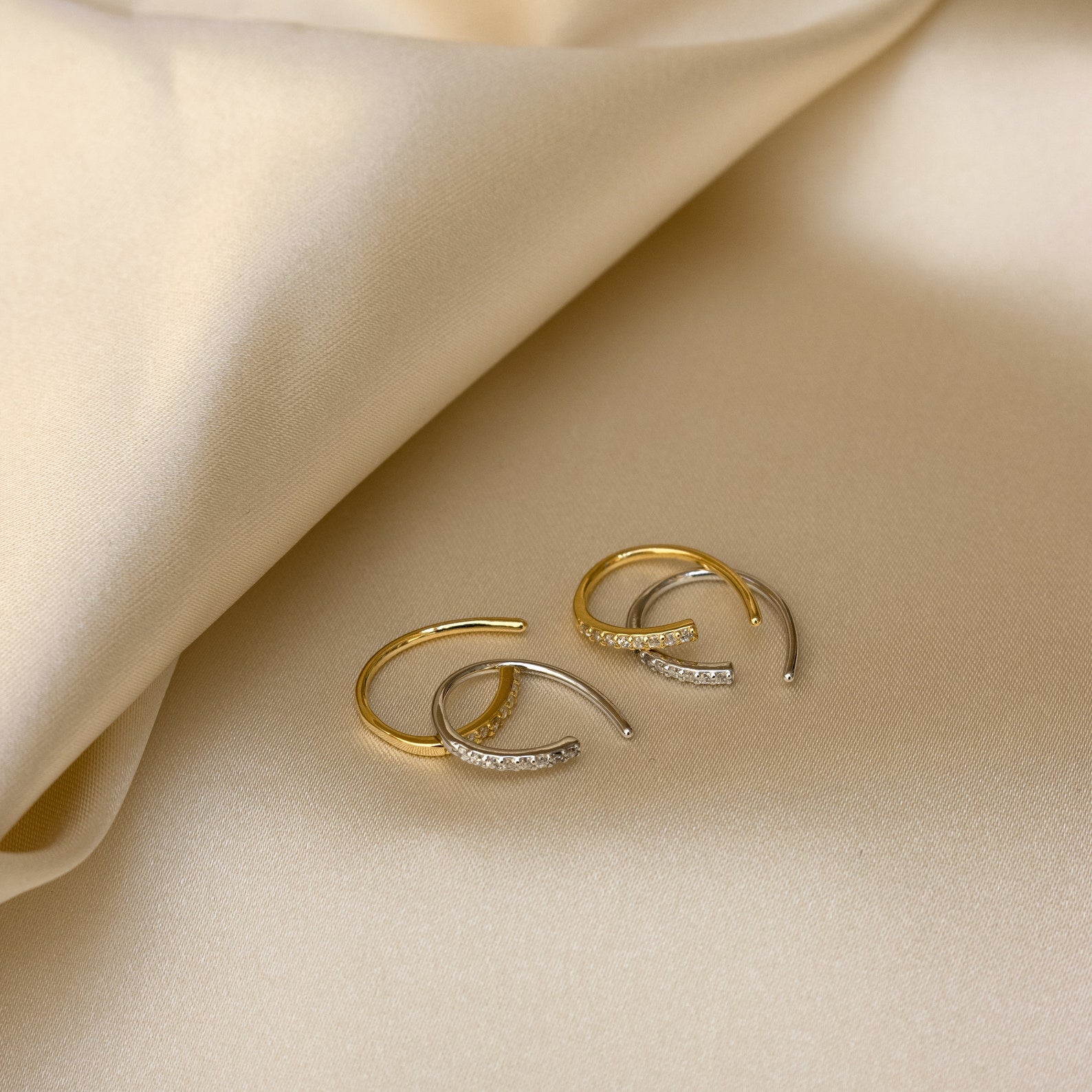 Pave Wire Diamond Hoops, featuring dainty gold and silver hoops with small crystals, displayed on smooth beige satin fabric.