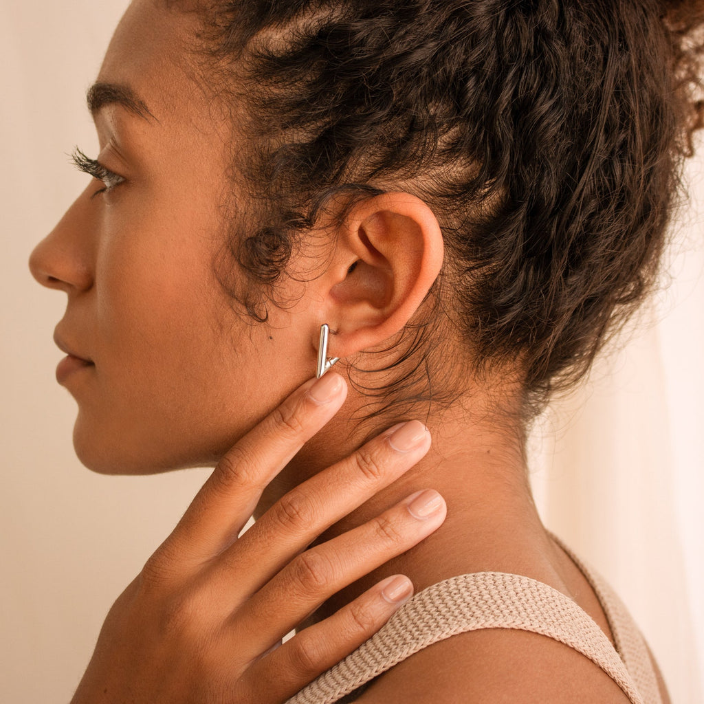 Woman with curly hair touches her neck, showcasing summer style in a textured tank top and Triangle Huggies earrings, side profile view.