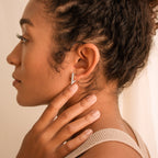 Woman with curly hair touches her neck, showcasing summer style in a textured tank top and Triangle Huggies earrings, side profile view.