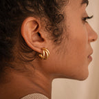 Close-up side view of a person wearing the Jenna Triple Hoops, a chunky gold modern earring, in their left ear.