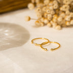 The adjustable Open Diamond Duo Ring in delicate gold rests on light fabric, with softly blurred dried flowers in the background—a perfect showcase of minimalistic jewelry.
