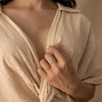 A woman in a beige textured shirt holds her collar, displaying two delicate gold rings including the Open Diamond Duo Ring—an elegant choice for minimalistic jewelry lovers.