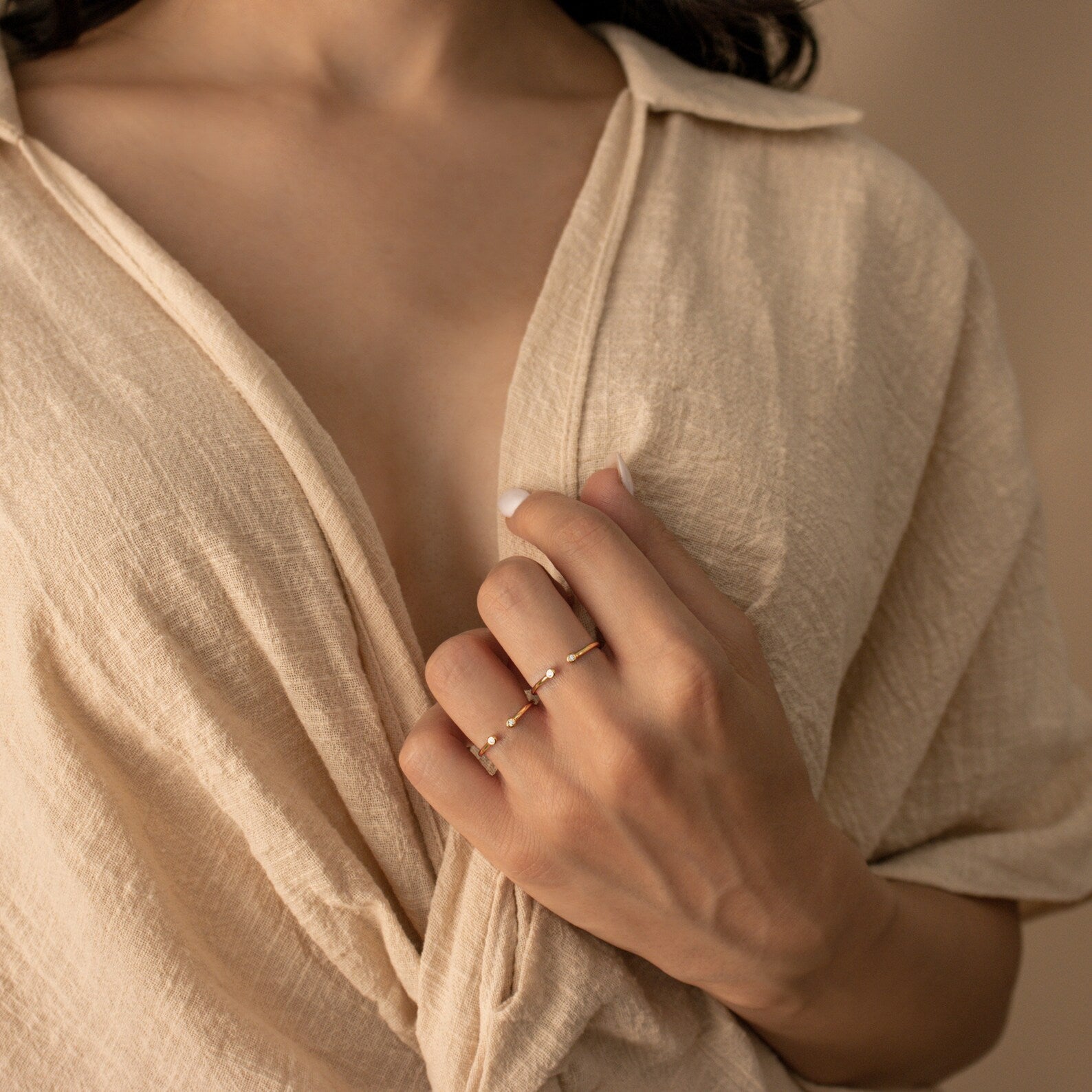 A woman in a beige textured shirt holds her collar, displaying two delicate gold rings including the Open Diamond Duo Ring—an elegant choice for minimalistic jewelry lovers.