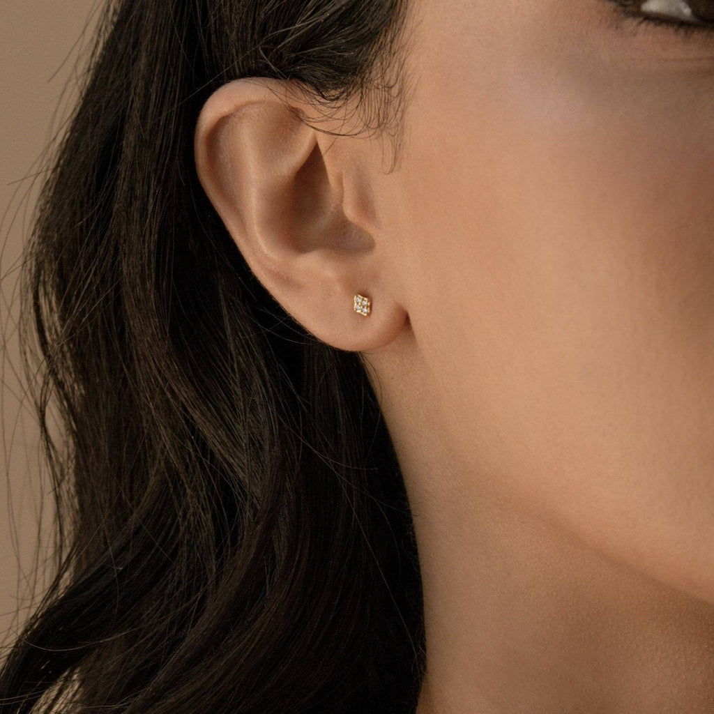 Close-up of a woman's ear wearing Avery Geometric Diamond Studs, small in size, with wavy dark hair partially visible.