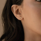 Close-up of a woman's ear wearing Avery Geometric Diamond Studs, small in size, with wavy dark hair partially visible.