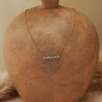 Gold necklace displayed on a terracotta surface, featuring a row of stacked, organic-shaped white beads arranged in a horizontal line at the center.