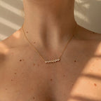 Close-up of a woman's neck wearing the Bethany Baguette Bar Necklace, a delicate gold cable chain with a small baguette bar pendant.