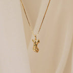 The Kinn Body Necklace features a gold pendant shaped like an abstract female torso, inspired by Venus de Milo, shown against a soft beige background.