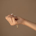A hand with manicured nails holds the Kinn Body Necklace, featuring a gold boot-shaped pendant that symbolizes empowerment, set against a beige background.