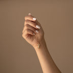 A manicured hand holds the Kinn Body Necklace, a gold Venus de Milo pendant symbolizing empowerment, against a beige background.