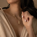 Woman wearing a gold chain necklace with a sculptural female form pendant featuring a shimmering iridescent inlay, styled with a neutral textured wrap top.