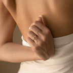 A woman in a white wrap shows her back, wearing the Love Heart Knot Ring—a delicate gold band that shines beautifully as a promise ring on her finger.