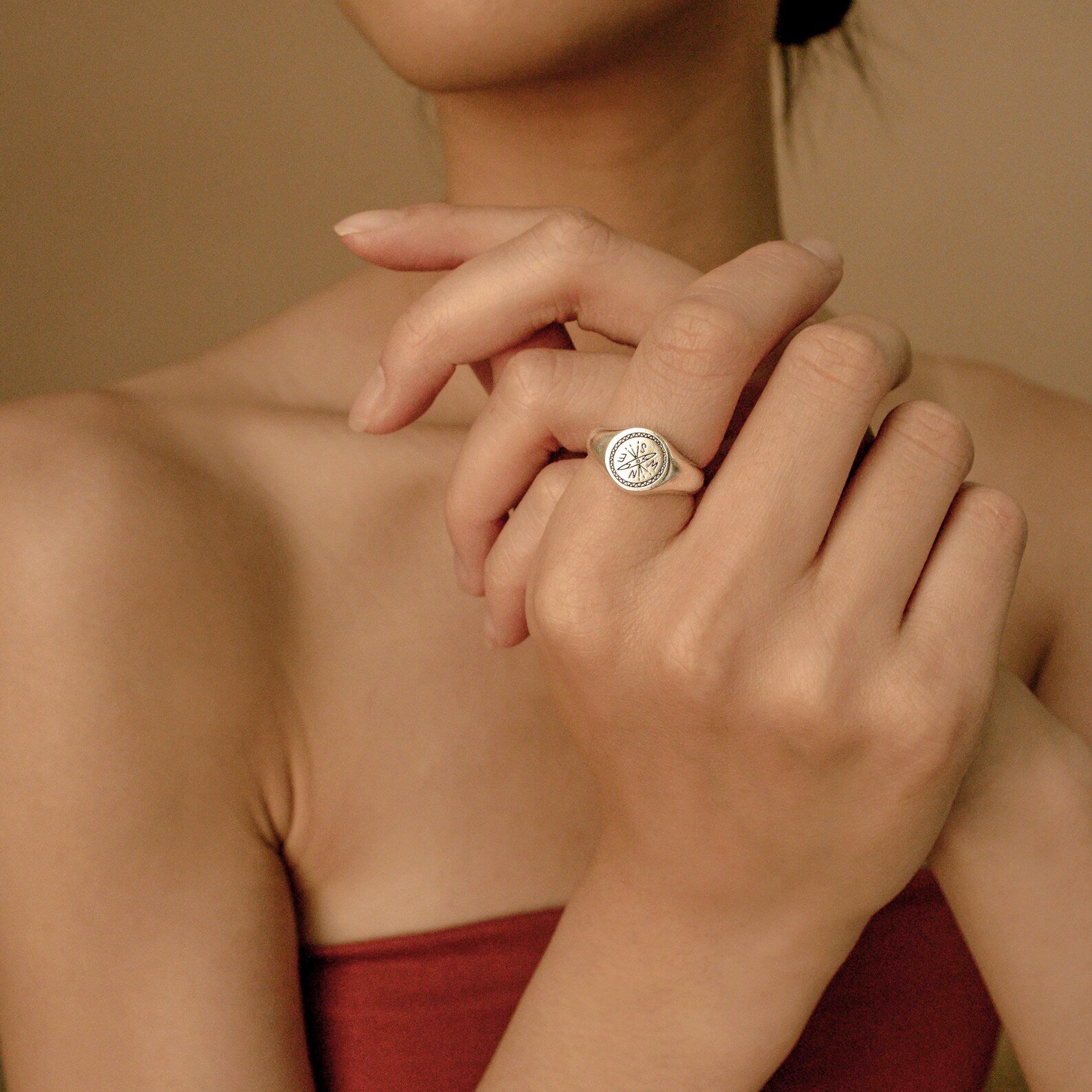 A woman elegantly crosses her hands, highlighting the Wanderlust Signet Ring with its tree design on her finger.