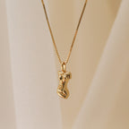 The Kinn Body Necklace features a gold pendant shaped like a stylized human torso, inspired by the Venus de Milo, displayed against a soft beige background—a refined and empowering jewelry piece.