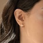 Close-up of a woman wearing Scarlett Pearl Huggies—gold hoops featuring a dangling mother of pearl heart charm.