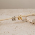 Two silver and two gold Madison Hoops are arranged on a wooden stick atop beige stone tiles—ideal for achieving a minimalist look.