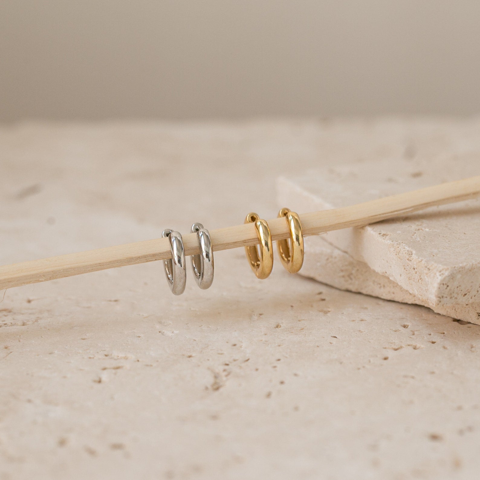 Two silver and two gold Madison Hoops are arranged on a wooden stick atop beige stone tiles—ideal for achieving a minimalist look.