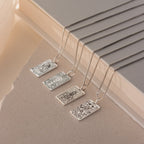 Four Tarot Necklace in Box Chain styles featuring rectangular Major Arcana pendants are displayed on a beige textured surface near books, perfect for adding mystique to your Tarot collection.