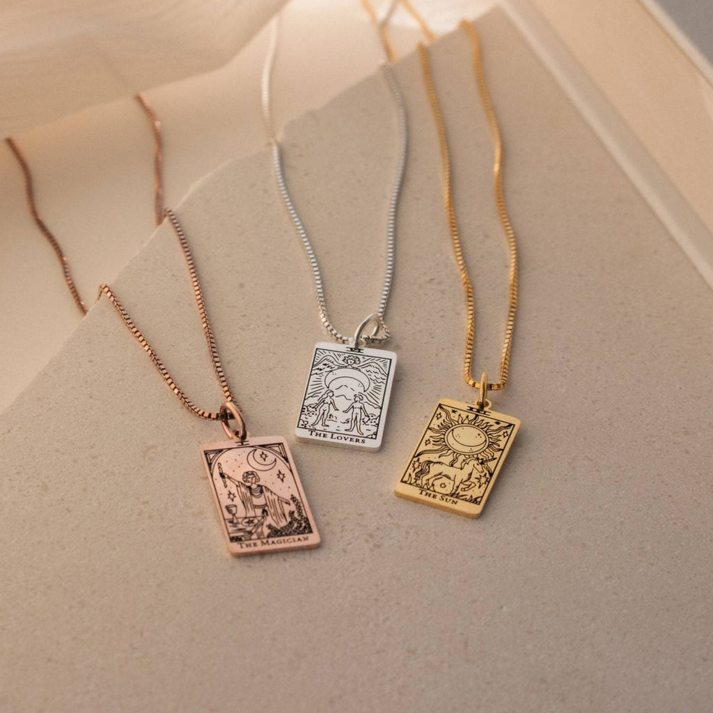 Three Tarot Necklace in Box Chain pieces from the Major Arcana collection—gold, silver, and rose gold—are displayed on a neutral surface.