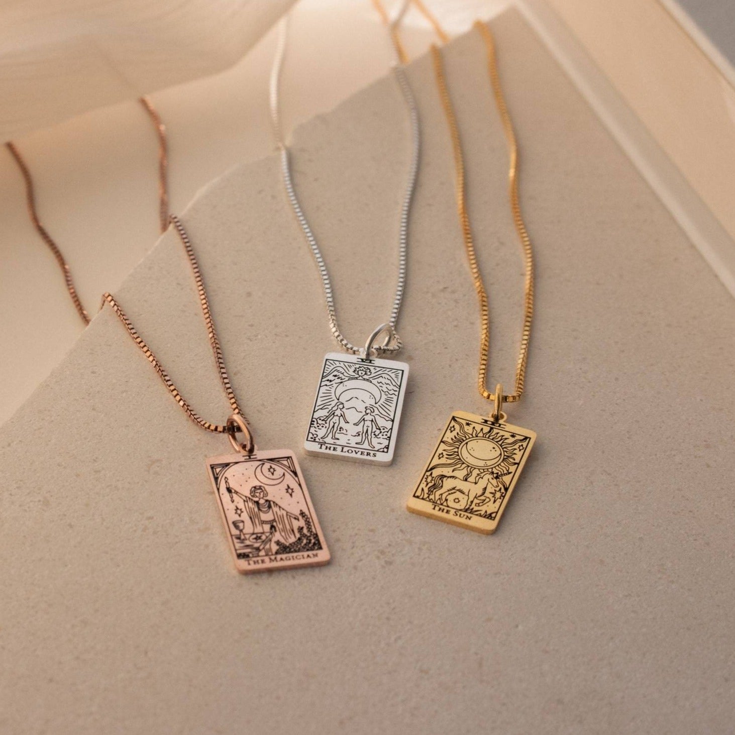 Three Tarot Necklace in Box Chain pieces from the Major Arcana collection—gold, silver, and rose gold—are displayed on a neutral surface.