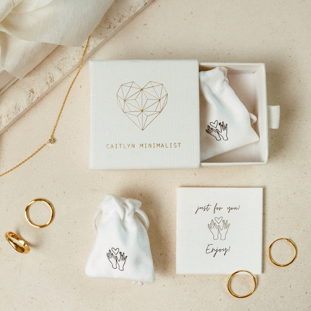 Old English Name Earrings come in a charming box with gold rings, a necklace, and small pouches on a beige surface—making them the perfect personalized gift.
